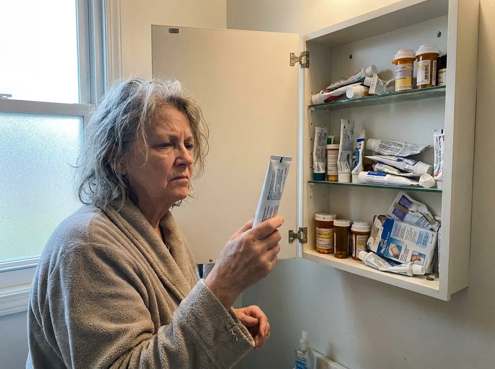 Woman reading a pain cream tube in front of a cabinet full of creams and pills